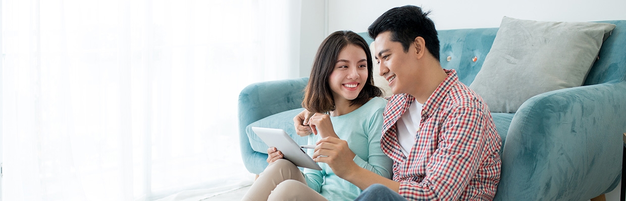 Asian couple at home discussing sitting on the floor and leaning against a blue couch